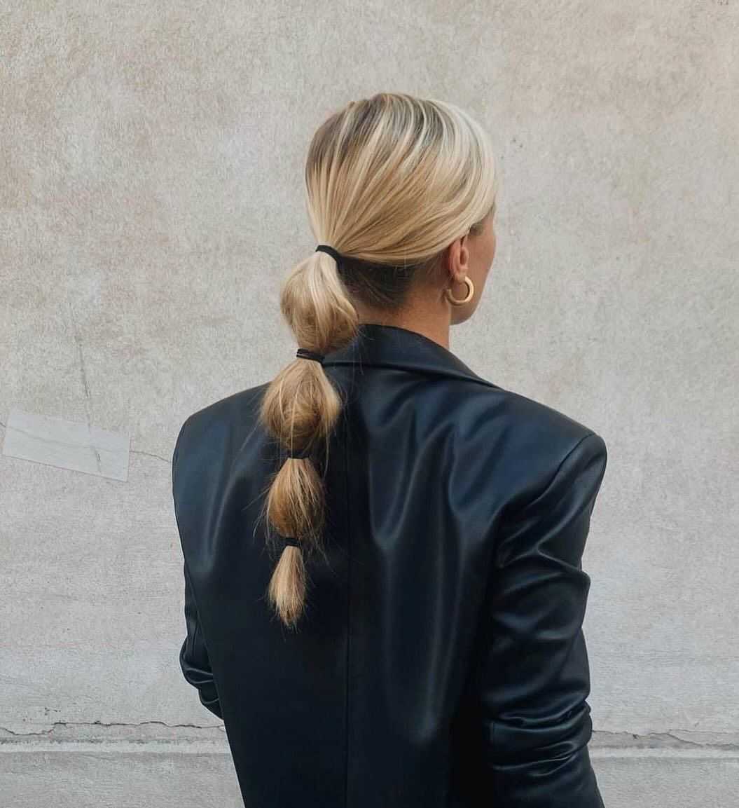 Woman with a stylish bubble ponytail wearing a black leather jacket, facing away from the camera.