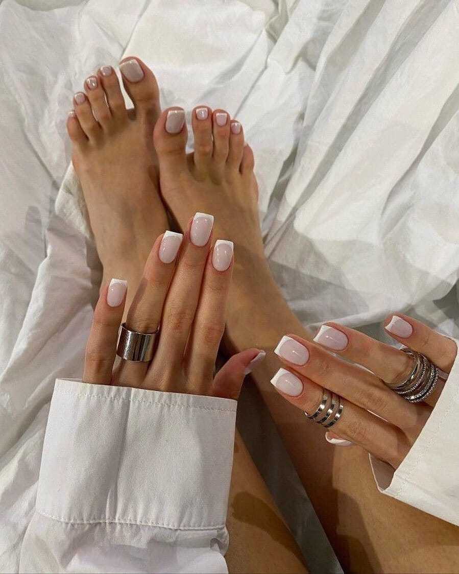 Hands and feet with manicured nails, adorned with rings, resting on white fabric.